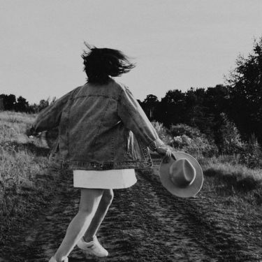 A young girl twirls joyfully outdoors on a sunny day, captured in black and white.